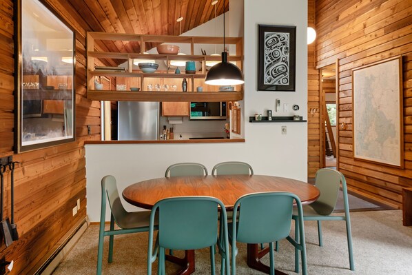 Un intérieur en bois comprenant une table à manger, des chaises, un coin cuisine et une grande fenêtre.