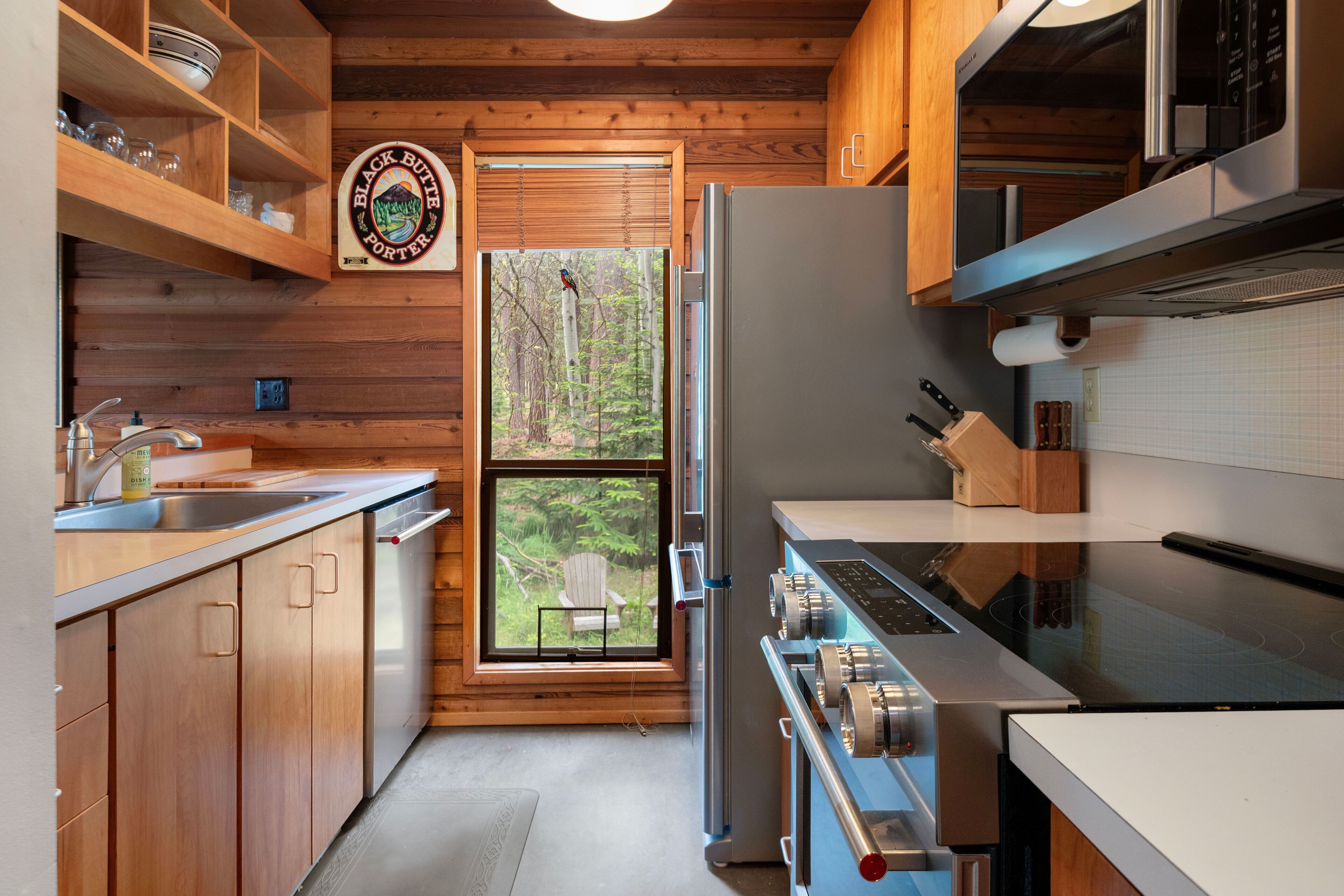 Une cuisine moderne avec des meubles en bois, un réfrigérateur en acier inoxydable et une grande fenêtre donnant sur une forêt.