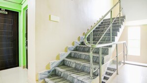 A staircase with marble steps and metal railings, a green door, and a light switch on the wall. - Hotel O Bolpur Central Railway Junction (Bolpur)