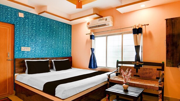 A hotel room with a bed, a ceiling fan, an air conditioning unit, a window with curtains, and a small table with a vase. - Hotel O Bolpur Central Railway Junction (Bolpur)