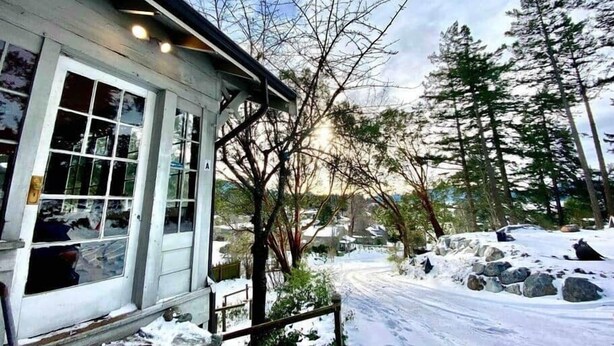 A snow-covered landscape with a building featuring a large window and a wooden porch. - Heart of Eastsound-For couples! (Eastsound)