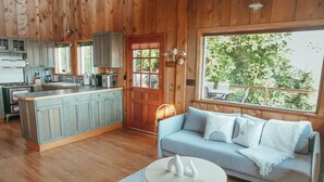 A cozy cabin interior with a kitchen, dining area, and a large window overlooking greenery. - INSANE VIEWS! HOT TUB! (San Juan County)