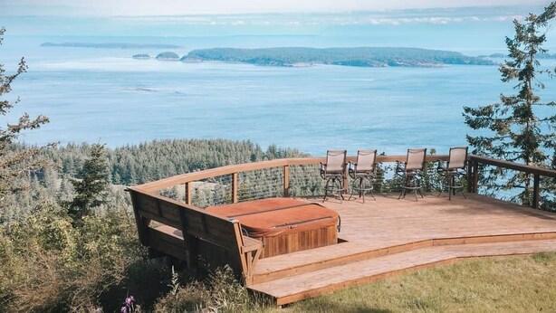A wooden deck with outdoor furniture overlooking a body of water and forested hills. - INSANE VIEWS! HOT TUB! (San Juan County)