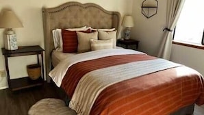 A bedroom with a bed, bedside tables, a lamp, a mirror, and a window with curtains.