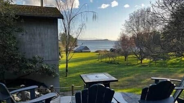 An outdoor seating area with tables and chairs facing a view of a body of water and trees.