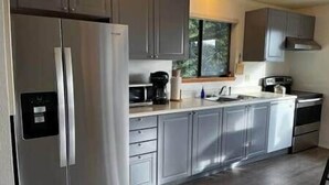 A modern kitchen with stainless steel appliances, grey cabinets, and a window providing natural light.