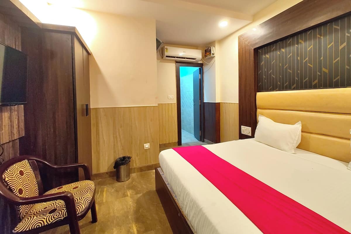 Een hotelkamer met een bed, een stoel, een airconditioning en een deur die naar een andere kamer leidt.
