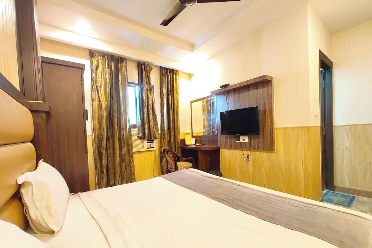 Een hotelkamer met een groot bed, een flatscreen televisie aan de muur, een bureau met stoel en een plafondventilator.