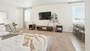 Een moderne woonkamer met een bank, salontafel, televisie en een eethoek met stoelen.