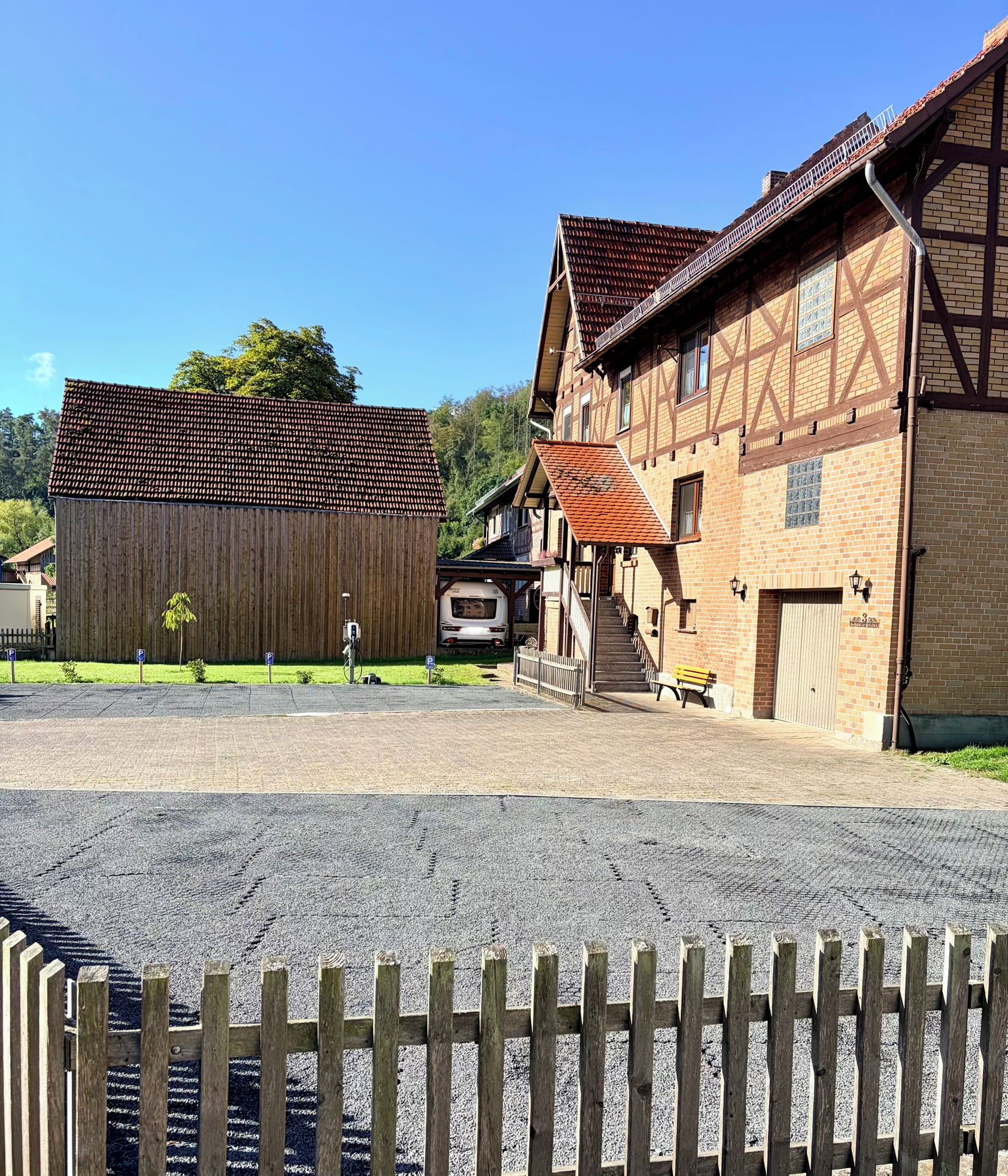 A traditional building with a sloped roof, a wooden fence, and a gravel driveway.