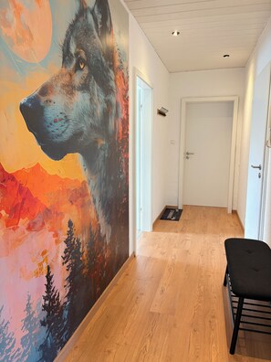 A hallway with a large wall mural of a wolf, wooden flooring, and a black bench. - Quiet, Nature-Filled Vacation Apartment - Little Red Riding Hood, with 3 bedrooms (Alheim)