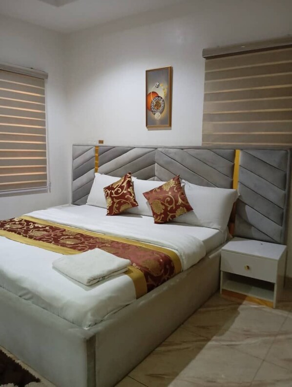 A neatly made bed with a patterned bedspread, two decorative pillows, a bedside table with a drawer, and a framed picture on the wall.