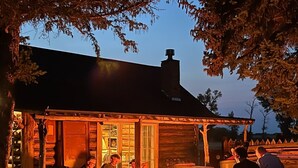 A rustic log cabin with a fire pit and people gathered around.