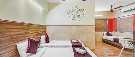 A hotel room with two beds, wooden headboards, a ceiling fan, a wall-mounted light, and a decorative wall piece.