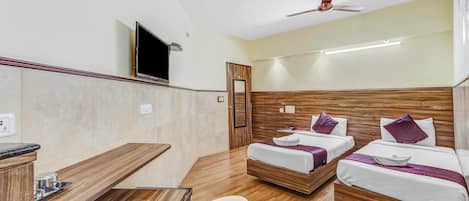 Ein Hotelzimmer mit zwei Betten, einem Fernseher, einem Deckenventilator und einem Holztisch.