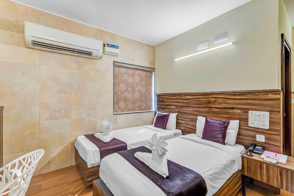 Une chambre d’hôtel avec deux lits, une tête de lit en bois, un appareil de climatisation, un téléphone sur la table de chevet et une petite table avec une lampe.