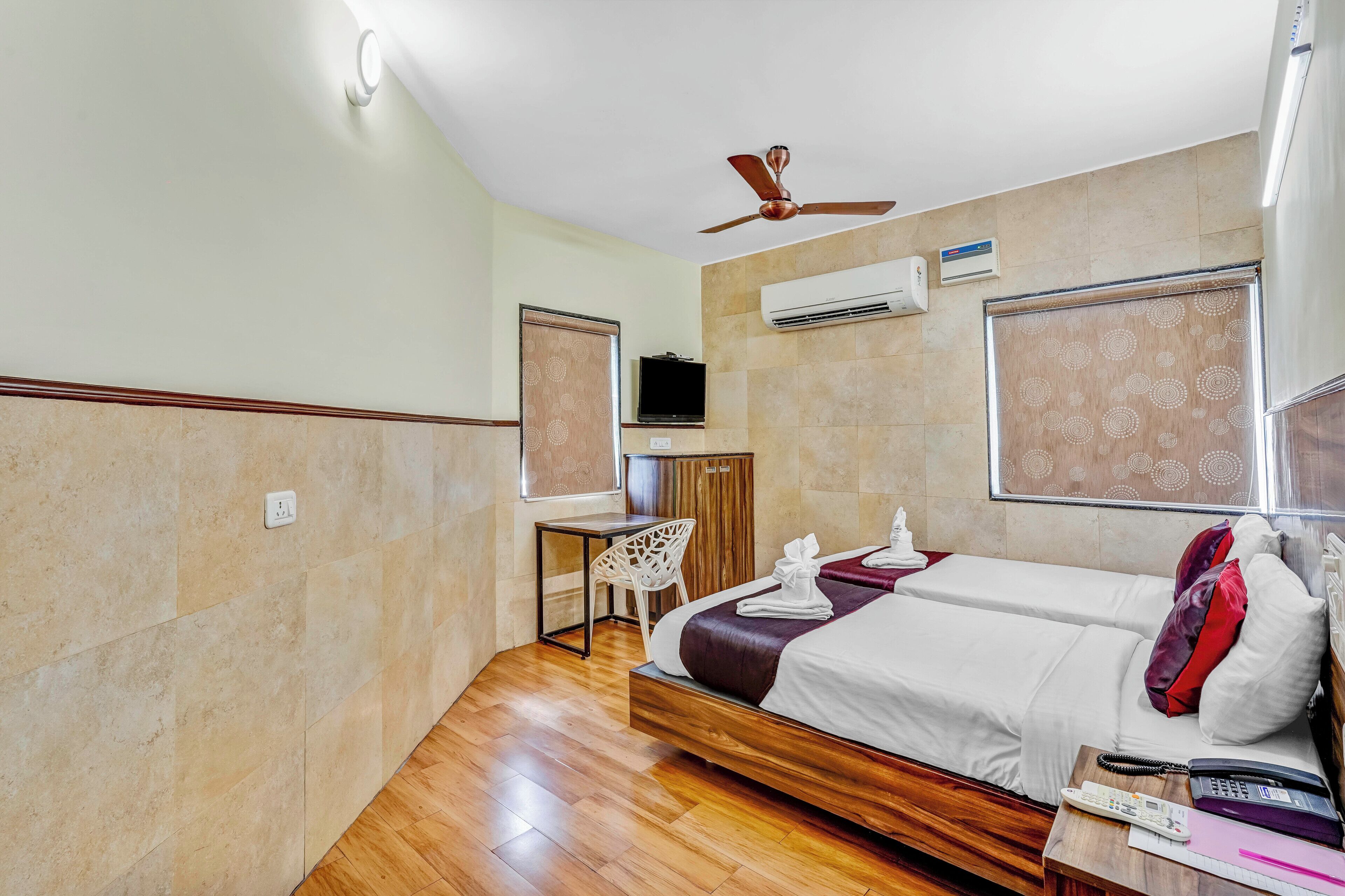 A hotel room with a bed, a desk, a chair, an air conditioning unit, and a television.