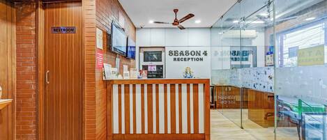A reception area with a wooden reception desk, a sign for 'Season 4 Reception', and a 'Restroom' sign on the left.