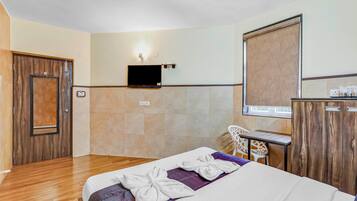 A hotel room with a bed, a TV mounted on the wall, a desk with a chair, and a wardrobe.
