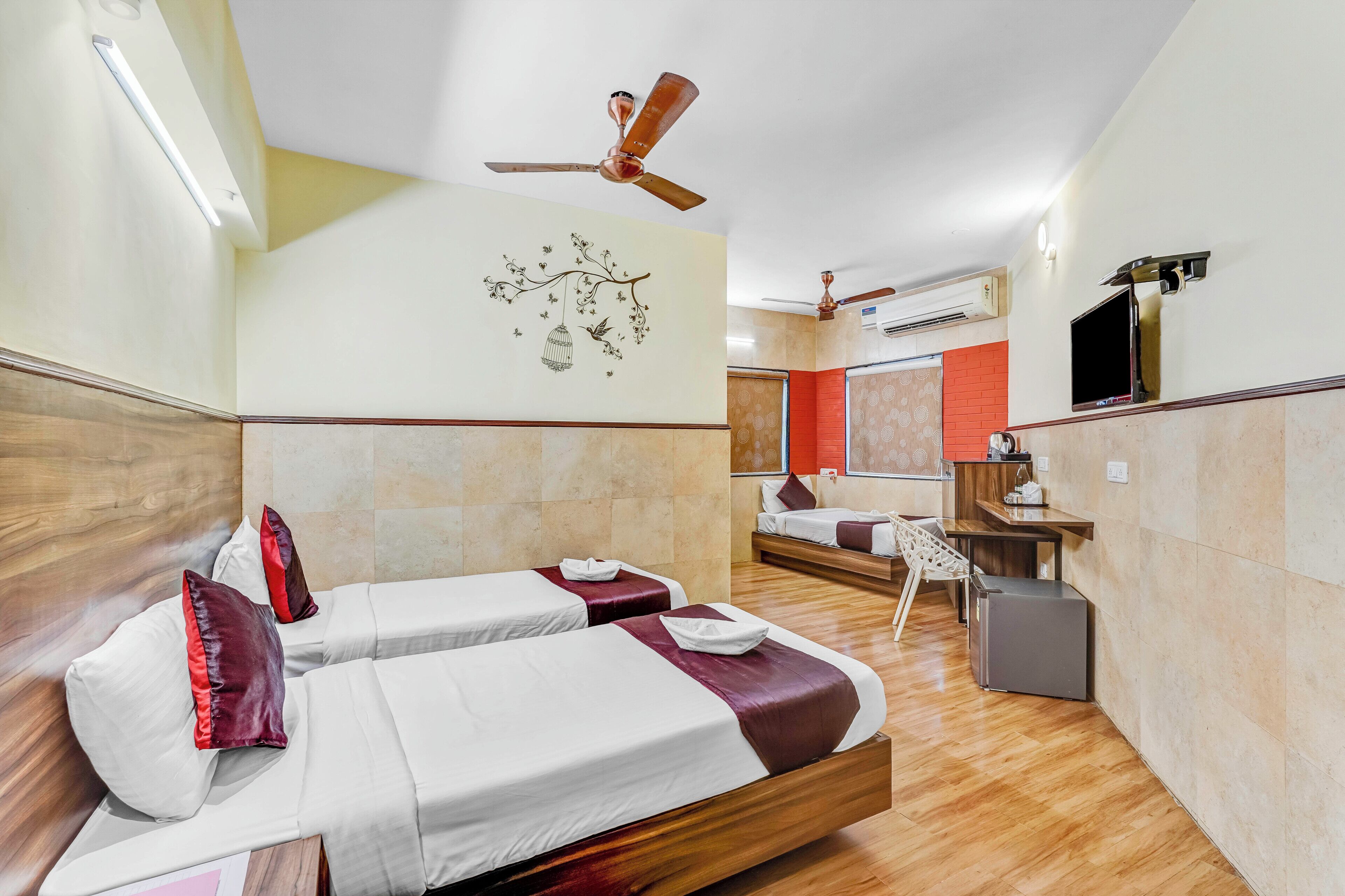 Una habitación de hotel con dos camas, un escritorio, una silla, un ventilador de techo y un televisor montado en la pared.