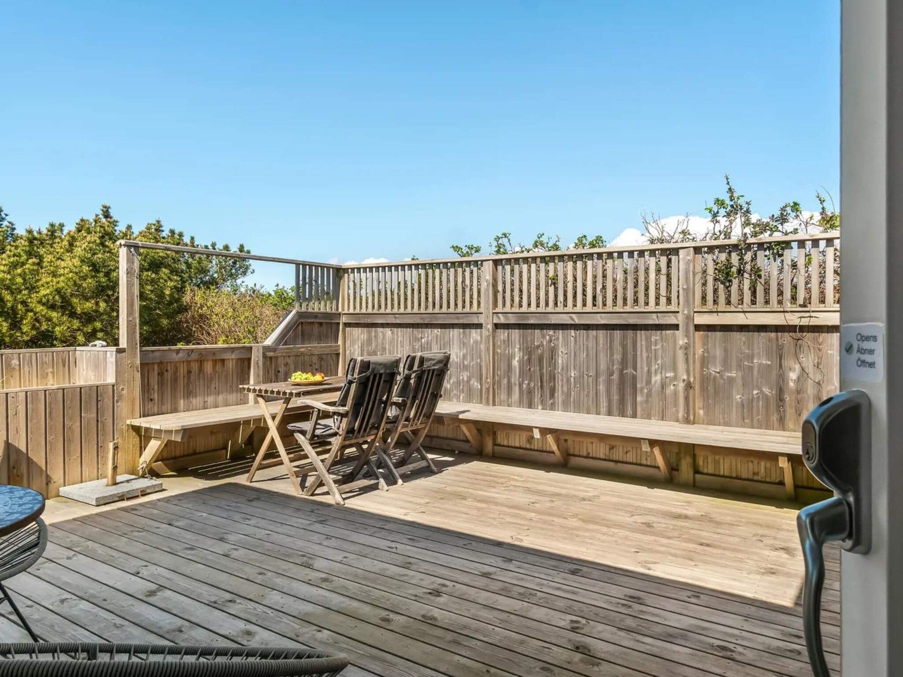 Une terrasse extérieure avec une table et des chaises en bois, une petite table ronde et une clôture en bois.