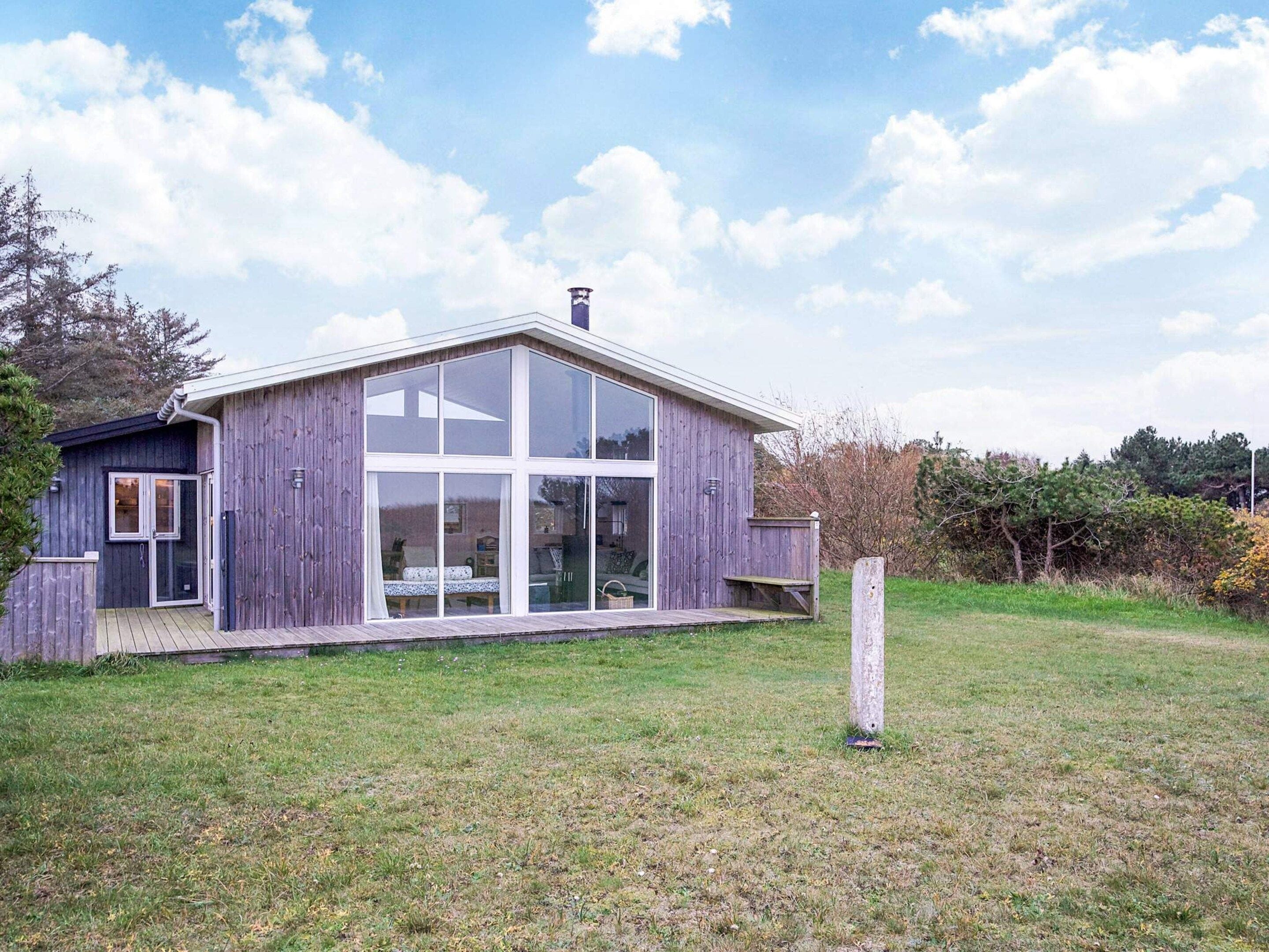 A modern wooden house with large glass windows and a deck.