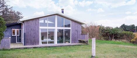 A modern wooden house with large glass windows and a deck.