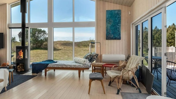 A cozy room with a large window, a sofa, a chair, and a fireplace.