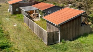 A wooden cabin with a red roof, a covered patio, and a view of the beach.