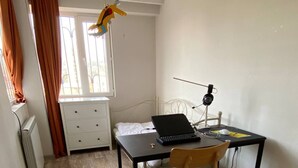 A room with a bed, a desk with a laptop, a chair, a radiator, and a window with curtains. - Charming apartment in marvelous Tbilisi with AC (Tbilisi)