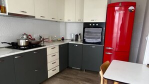 A compact kitchen with grey cabinets, a red refrigerator, a white pendant light, and a dining table with a chair. - Charming apartment in marvelous Tbilisi with AC (Tbilisi)