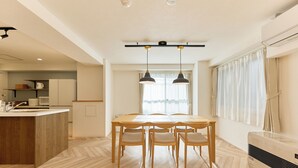 Una cocina moderna con una isla de madera, una mesa de comedor con sillas, luces colgantes y un amplio ventanal con cortinas.
