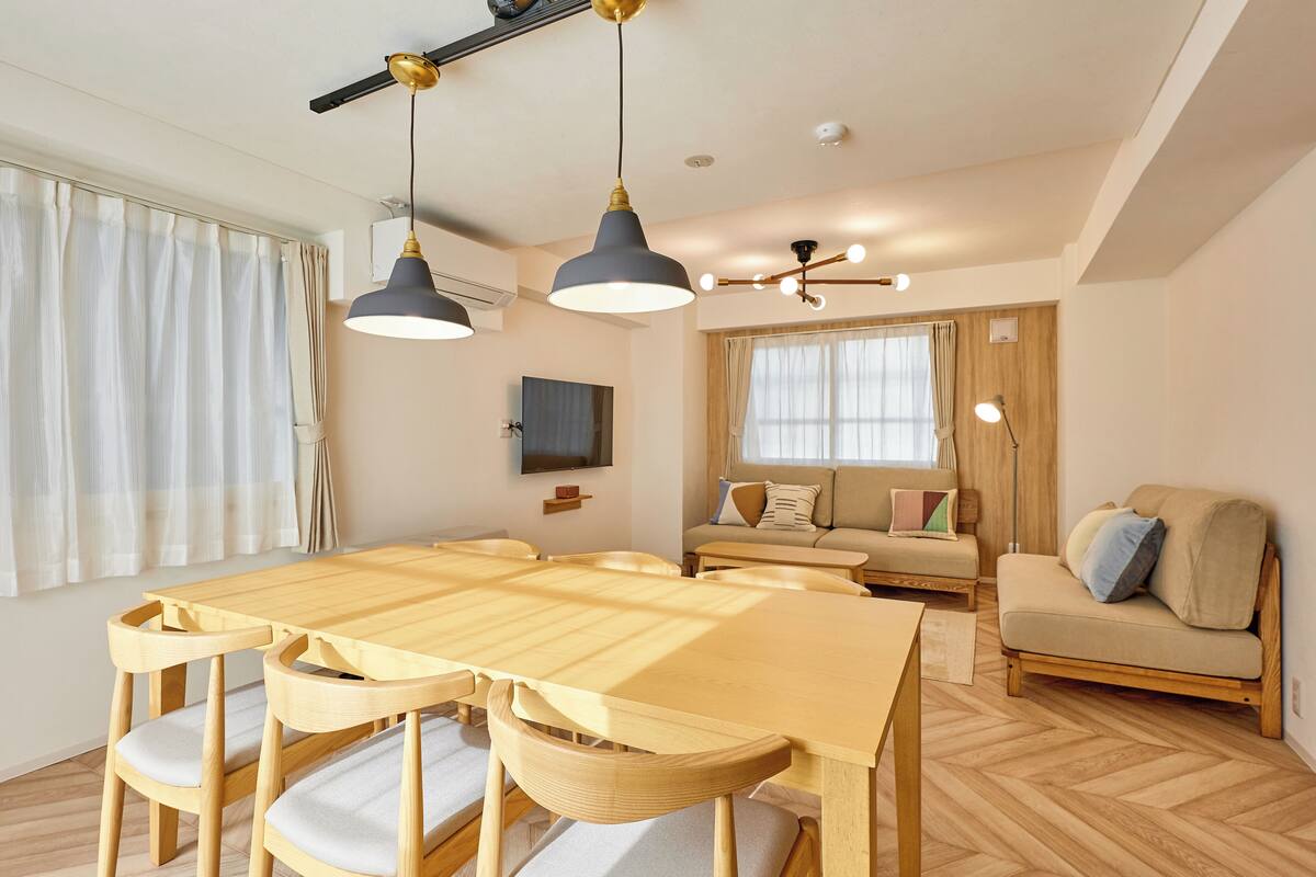 A modern living room with a wooden dining table, two chairs, a sofa, and a TV mounted on the wall.