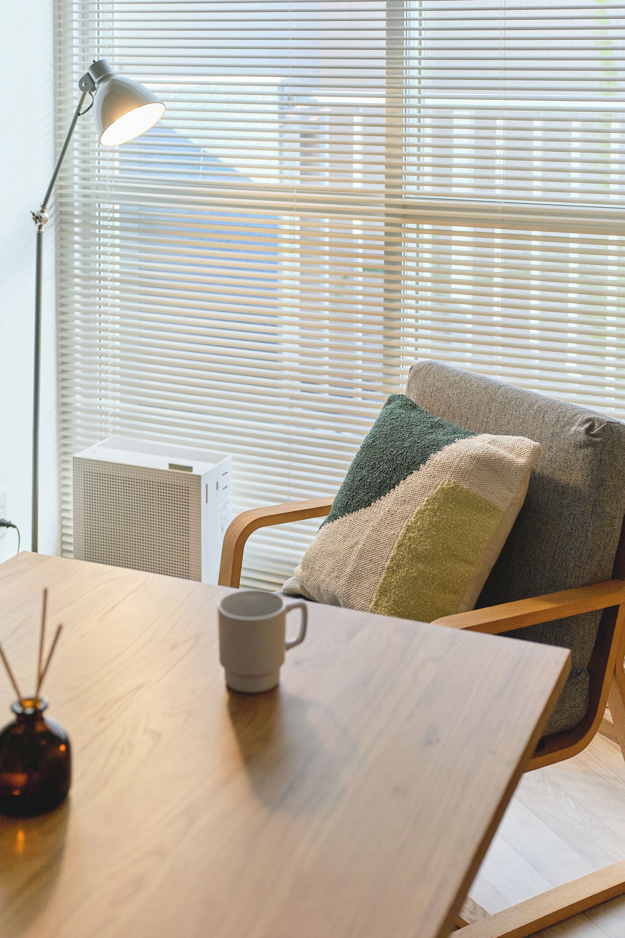 Een kamer met een houten tafel, een lamp, een radiator en een raam met zonwering.