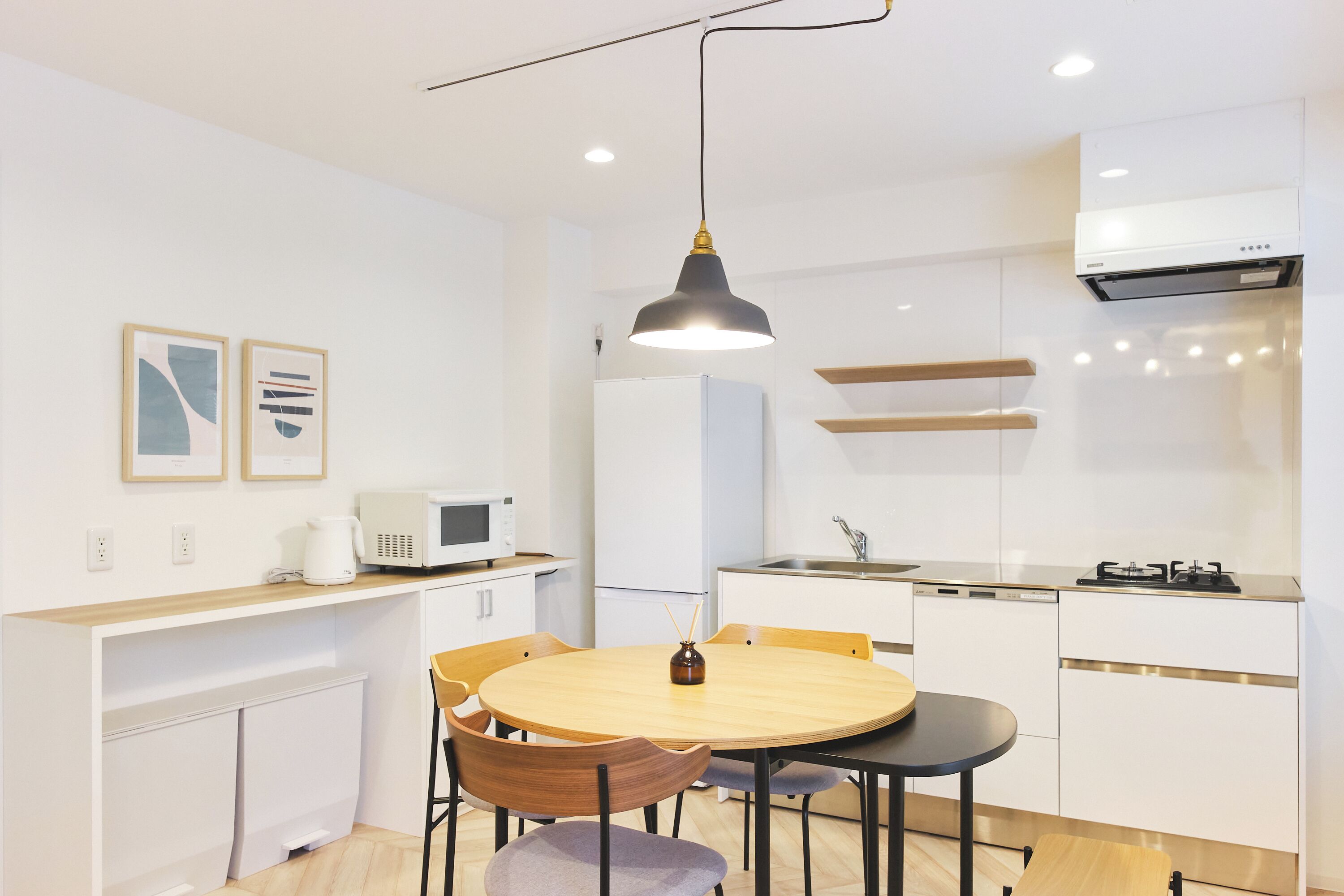 A modern kitchen with white cabinetry, a round wooden table, and a pendant light.