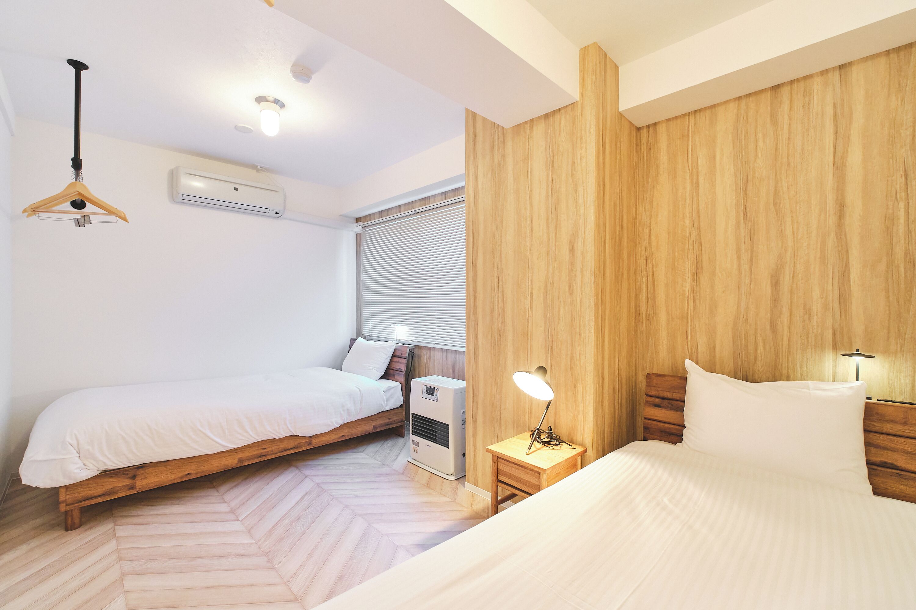 A bedroom with two single beds, a wooden headboard, a bedside table with a lamp, an air conditioning unit, and a hanging light fixture.
