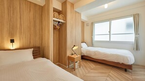 Habitación de hotel con dos camas, paneles de madera, una mesita de noche con lámpara, un estante con toallas dobladas y un amplio ventanal con cortinas.