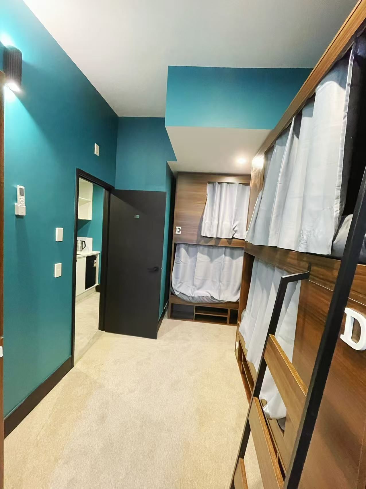 Una habitación con paredes color turquesa, una cama litera, una puerta que da a un baño y una pequeña kitchenette.