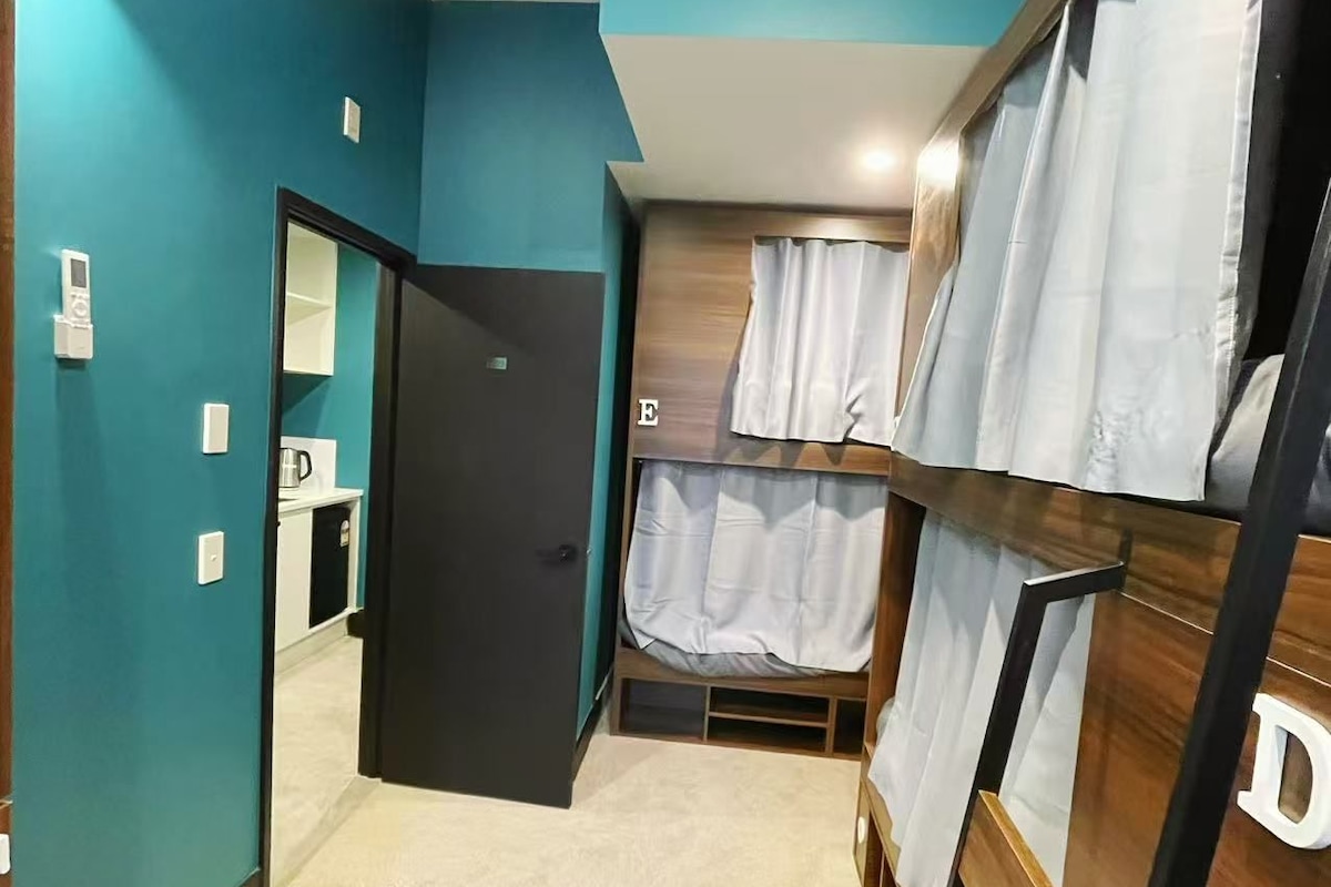 Ein Zimmer mit türkisfarbenen Wänden, einem Etagenbett, einer Tür zu einem Badezimmer und einer kleinen Küchenzeile.
