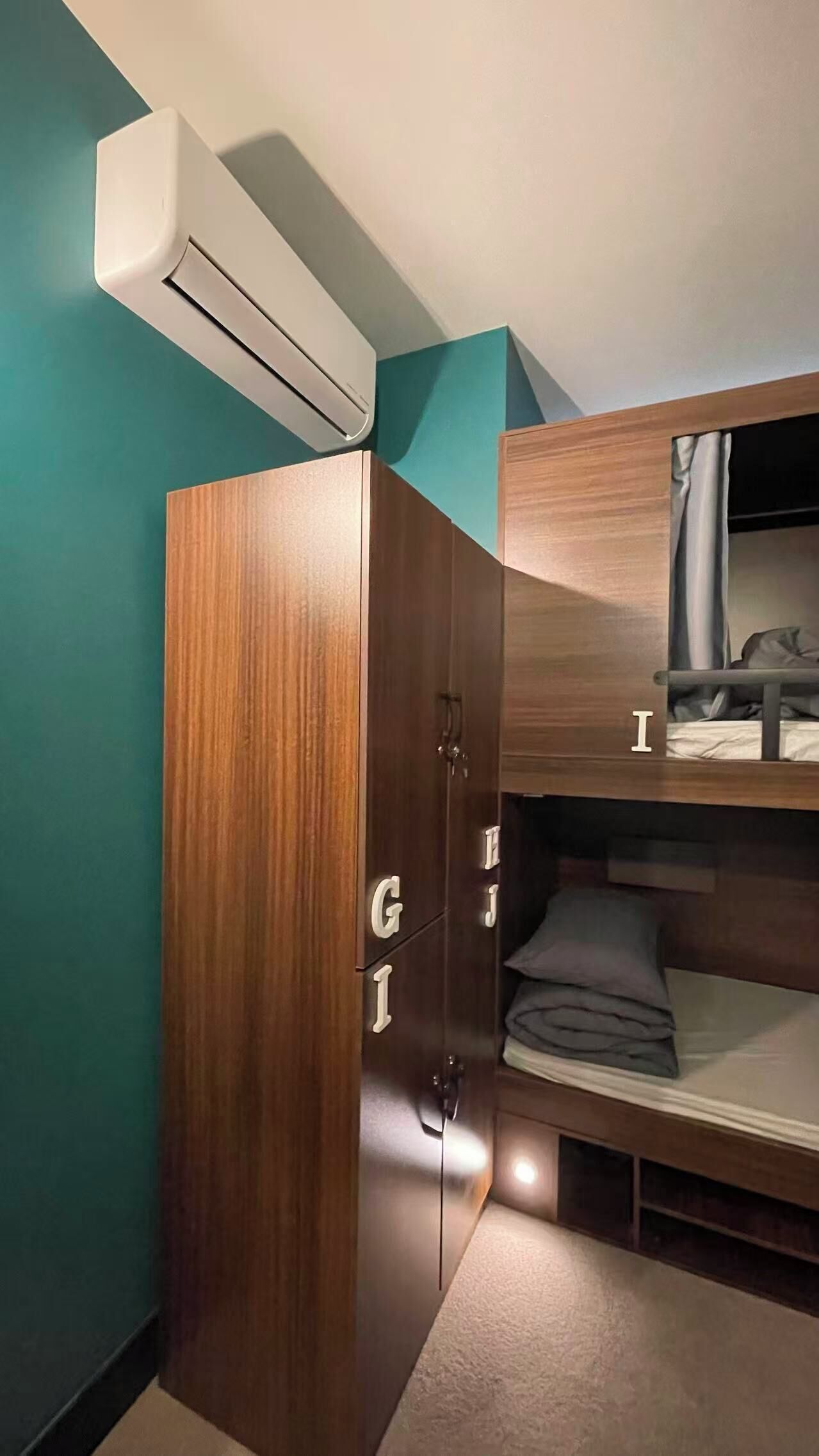 A compact room with a bunk bed, a wardrobe with drawers, and an air conditioning unit.