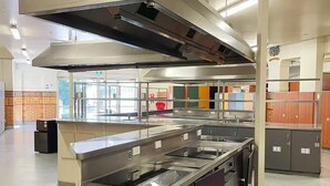 A commercial kitchen with stainless steel appliances, a central island, and a large exhaust hood. - Georgie Accommodation (Auckland)