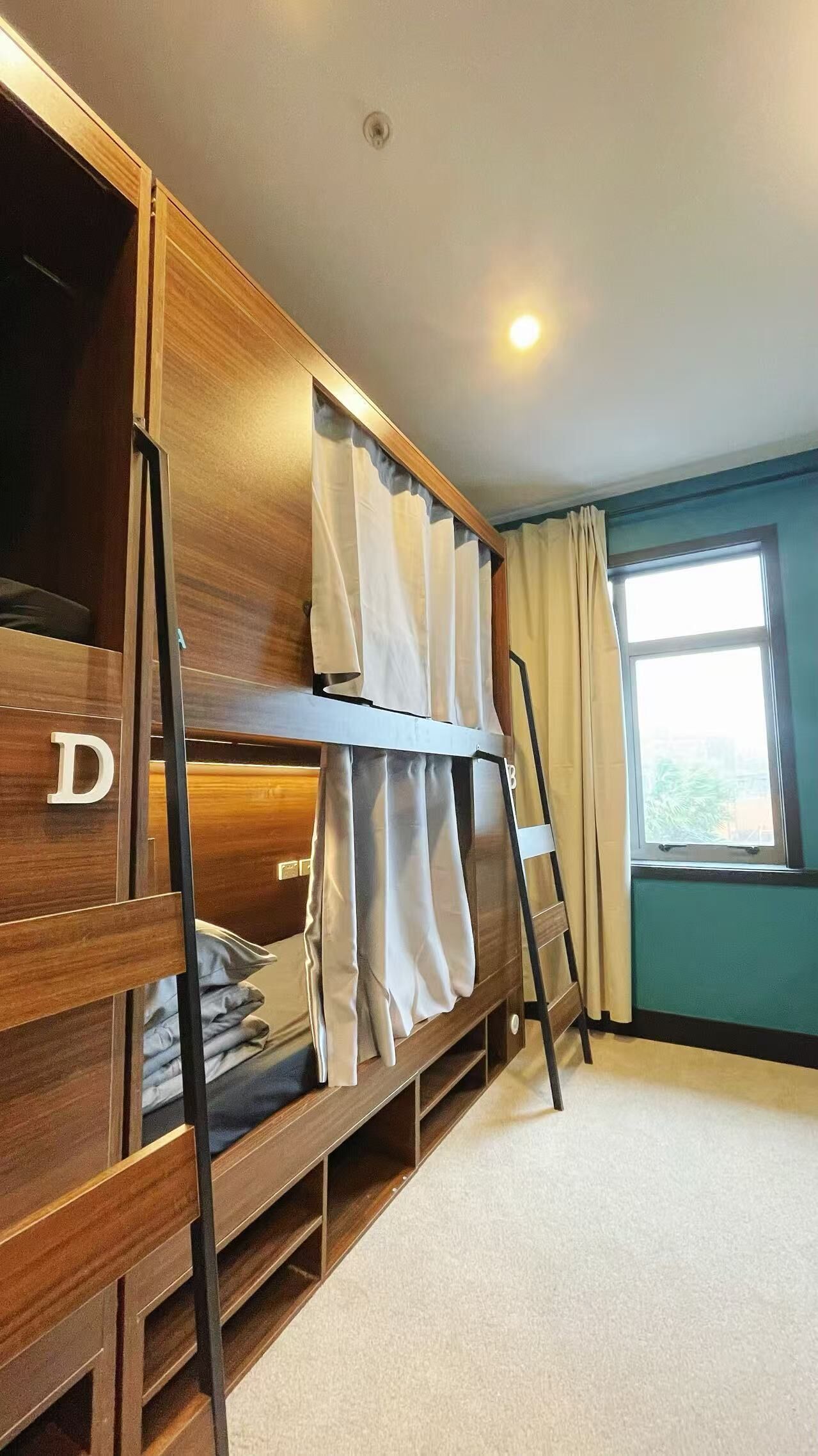 Une chambre avec un lit superposé, une échelle, une fenêtre avec des rideaux et un luminaire visible au plafond.