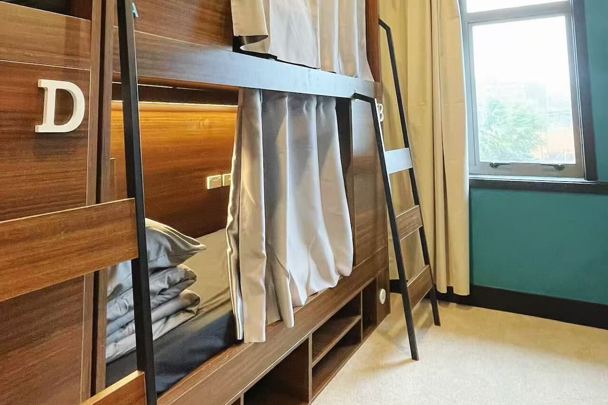 Une chambre avec un lit superposé, une échelle, une fenêtre avec des rideaux et un luminaire visible au plafond.