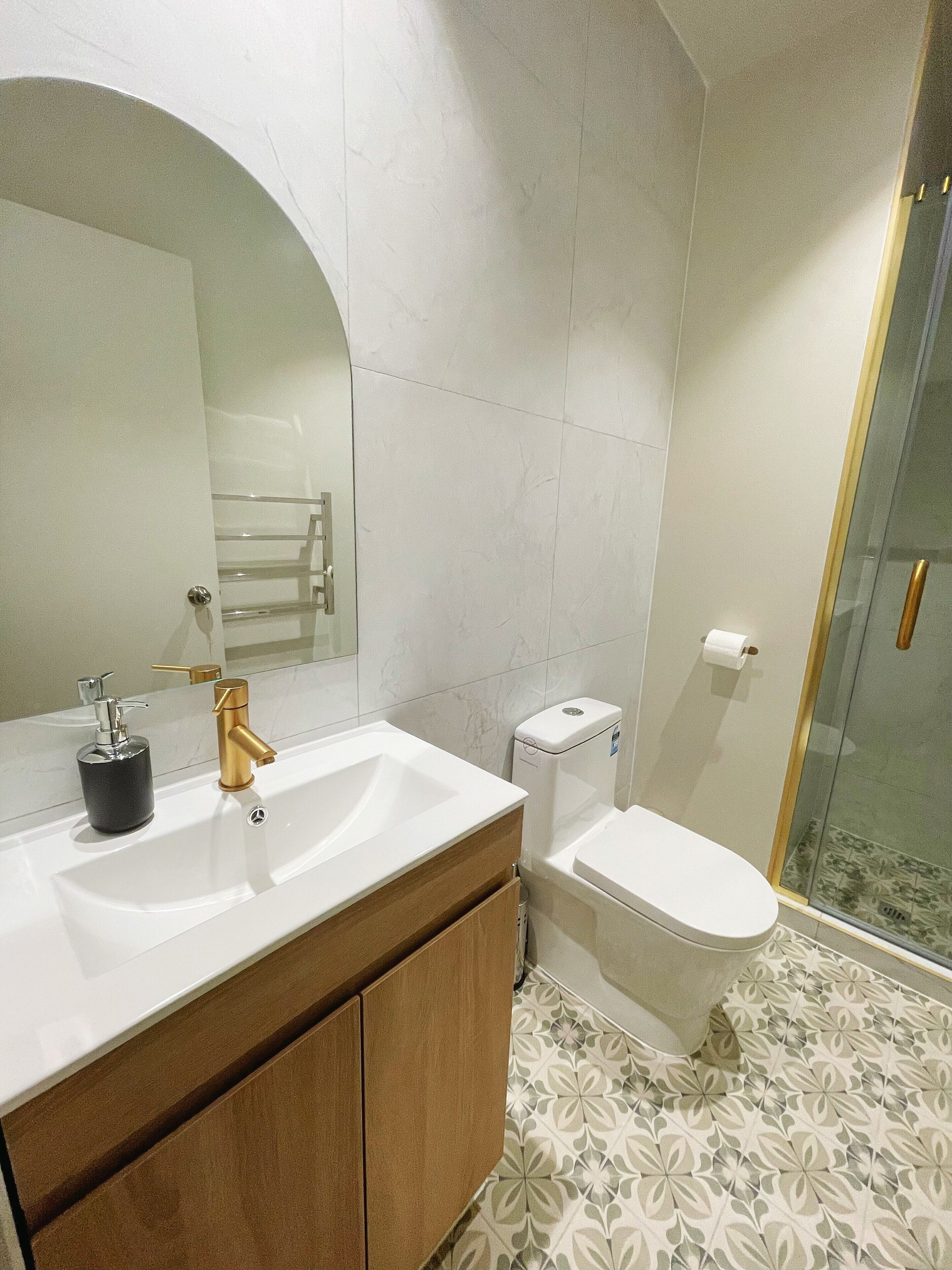 Un baño moderno con lavamanos blanco, grifo dorado y un espejo grande.