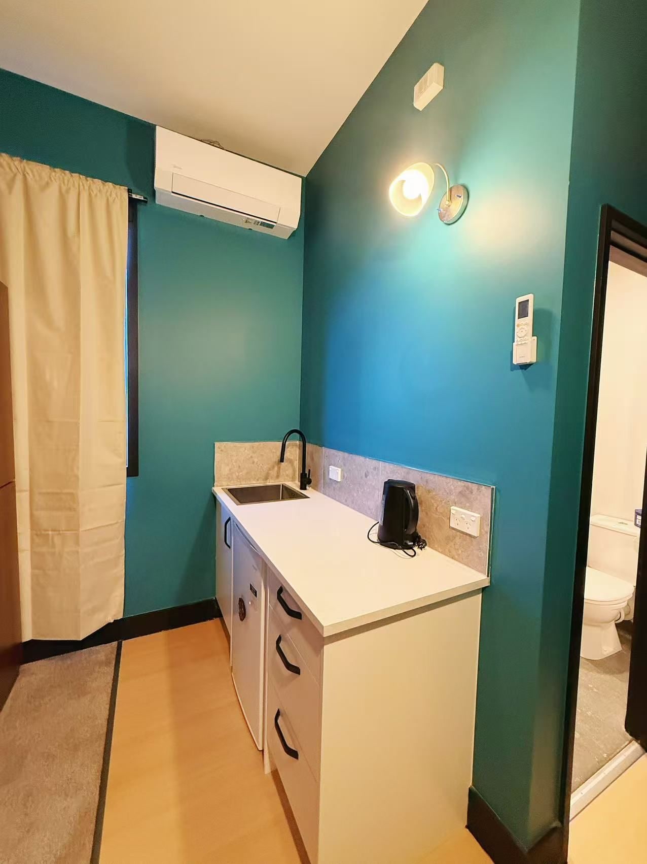 A compact kitchenette with a sink, a coffee maker, and a wall-mounted light fixture.