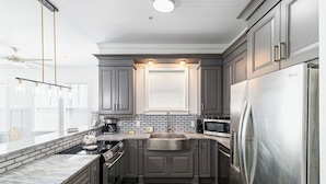 A modern kitchen with dark gray cabinets, stainless steel appliances, and a marble countertop.