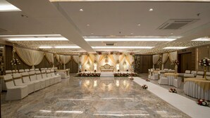 A spacious banquet hall with a central stage, rows of white chairs, and floral decorations. - Hotel Silvera Grand (Ahmedabad)
