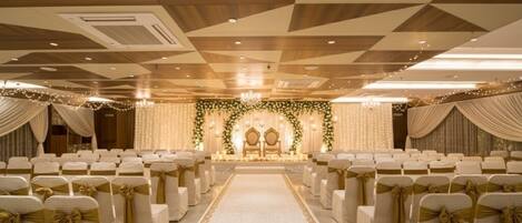 A banquet hall with rows of chairs, a stage with floral decorations, and a chandelier.
