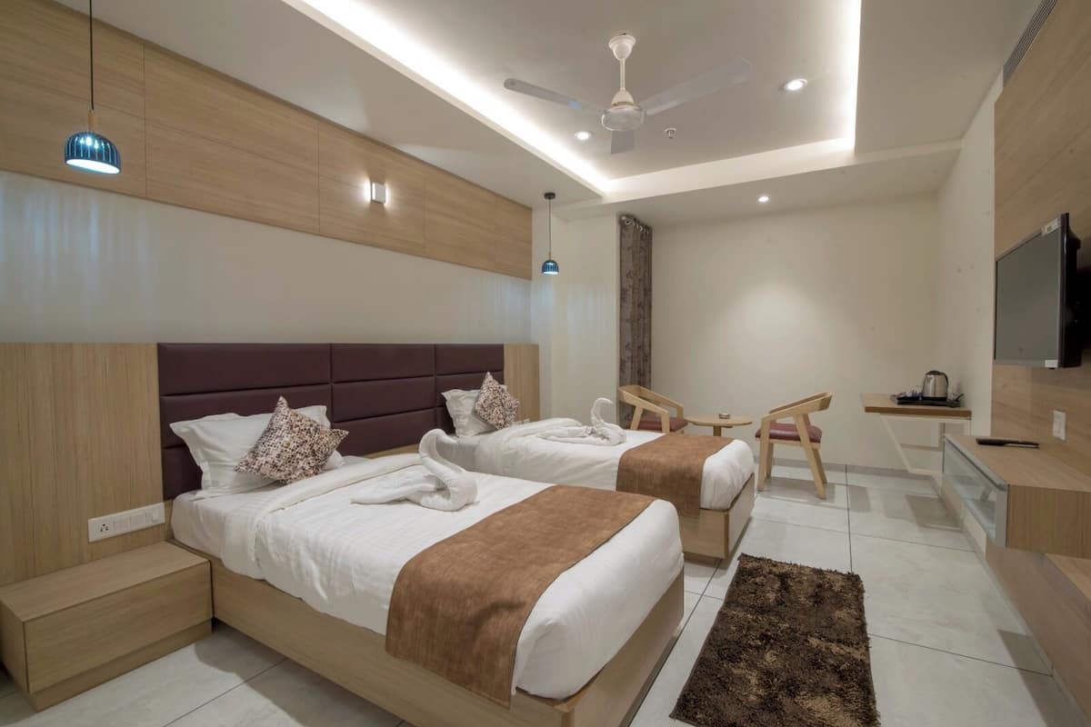 Ein modernes Hotelzimmer mit zwei Betten, einem Schreibtisch, einem Sessel, einem Fernseher und einem Deckenventilator.