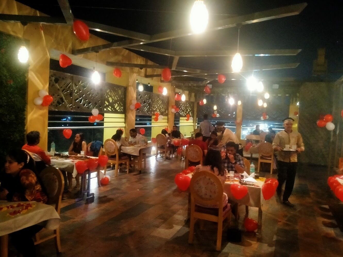 An indoor dining area with tables and chairs, decorated with red and white balloons.
